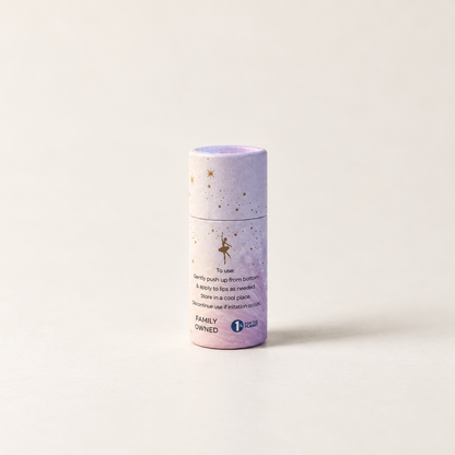 A small cylindrical lavender and white container with gold speckles and fairy illustrations, standing upright on a clean off-white background. The label includes the text 'FAMILY OWNED' and a one percent for the planet logo.